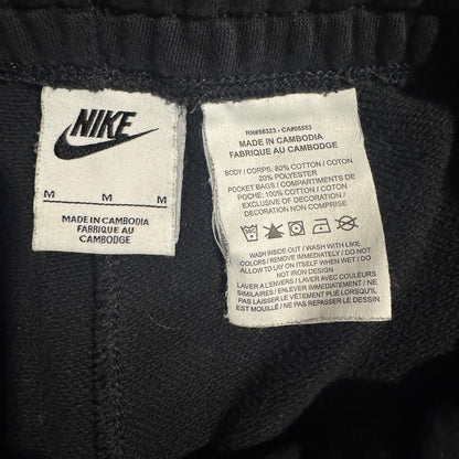 Close-up of a black Nike garment showing two white woven labels: one with the Nike logo and size information, and one with care instructions and product code PHMS8233 - CARNAGE53.