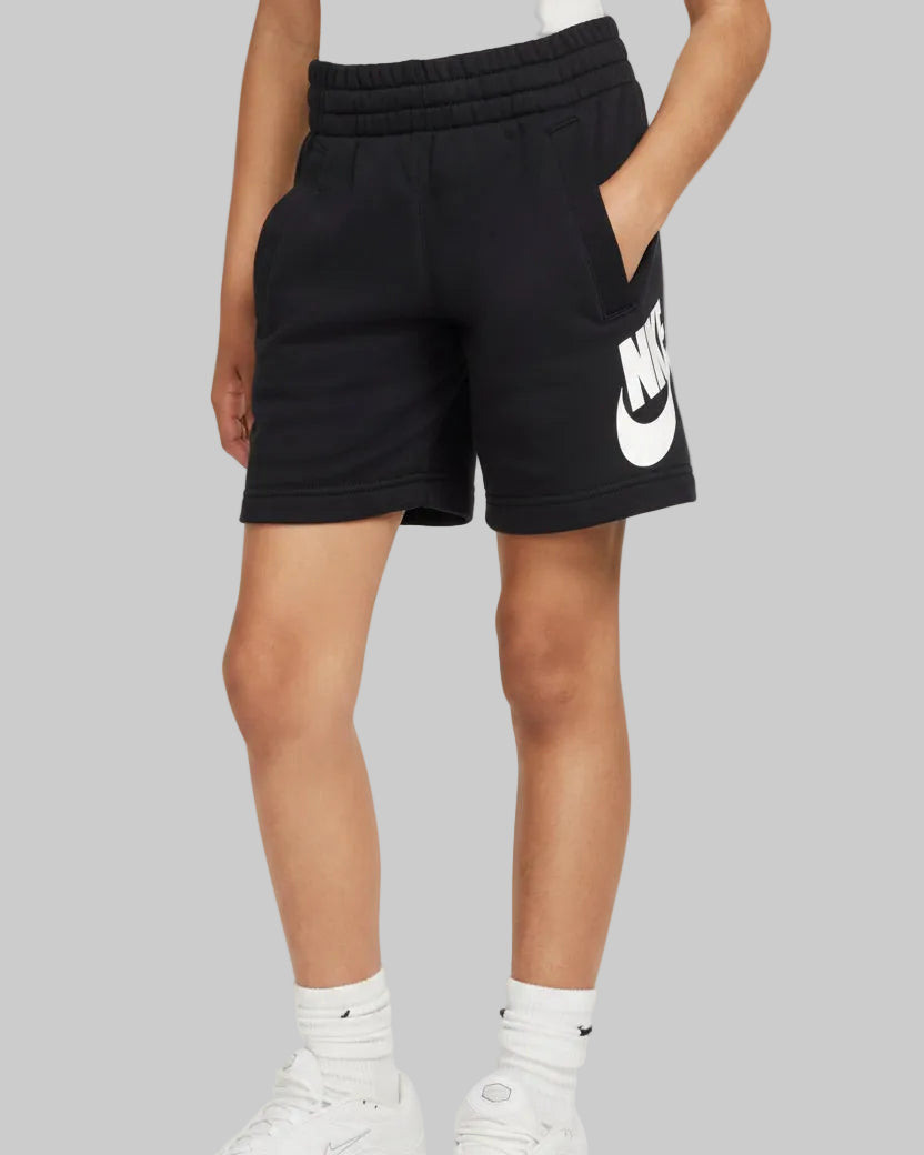 A model wearing black Nike athletic shorts with a large white logo on the left leg, paired with white socks and sneakers, against a light gray studio background.