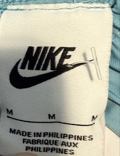 Close-up of a Nike garment tag with the black Nike logo and size information on a white fabric label, with a light blue garment visible around it.