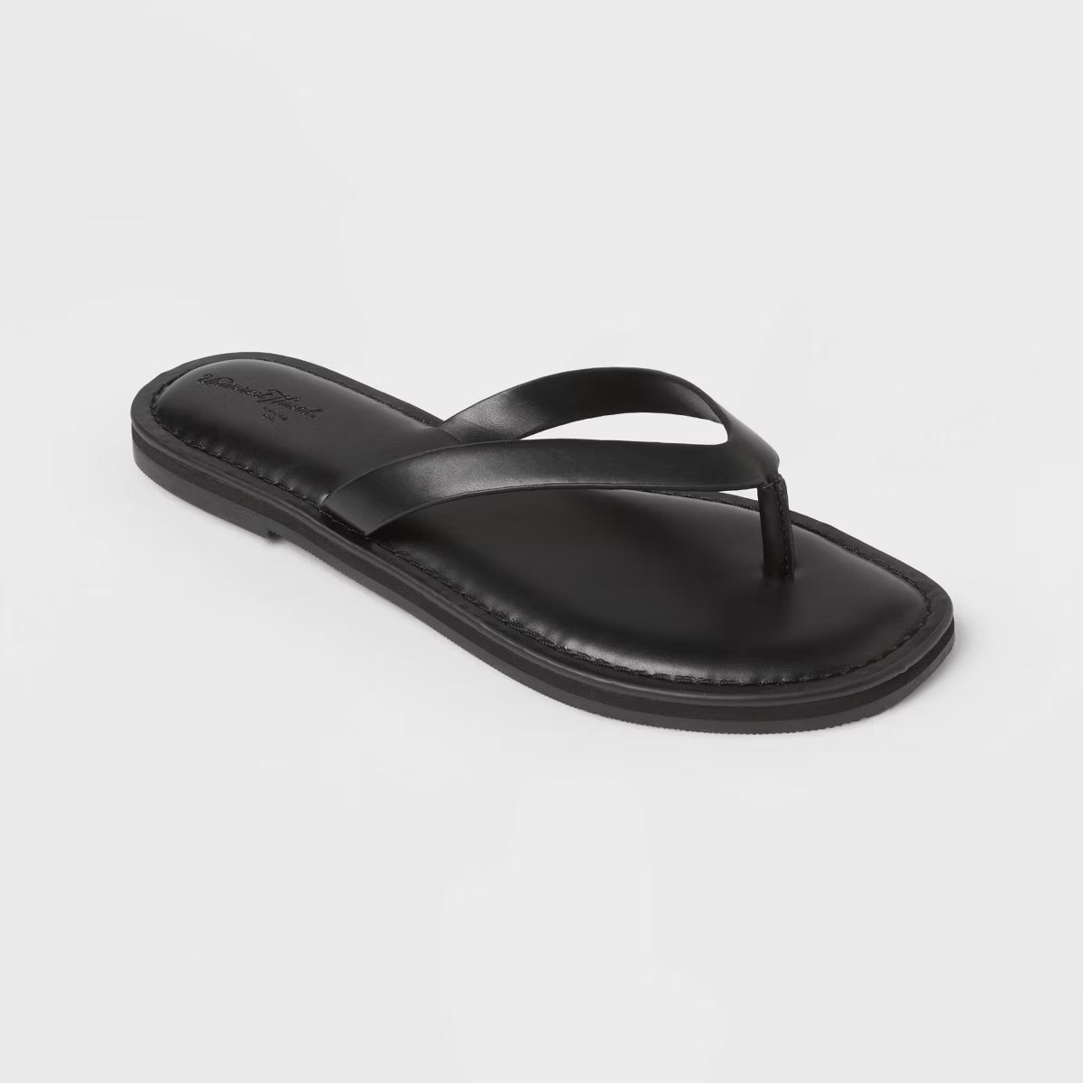 A single black leather thong sandal with a matching flat sole, photographed from a high-angle perspective against a clean, light gray background.