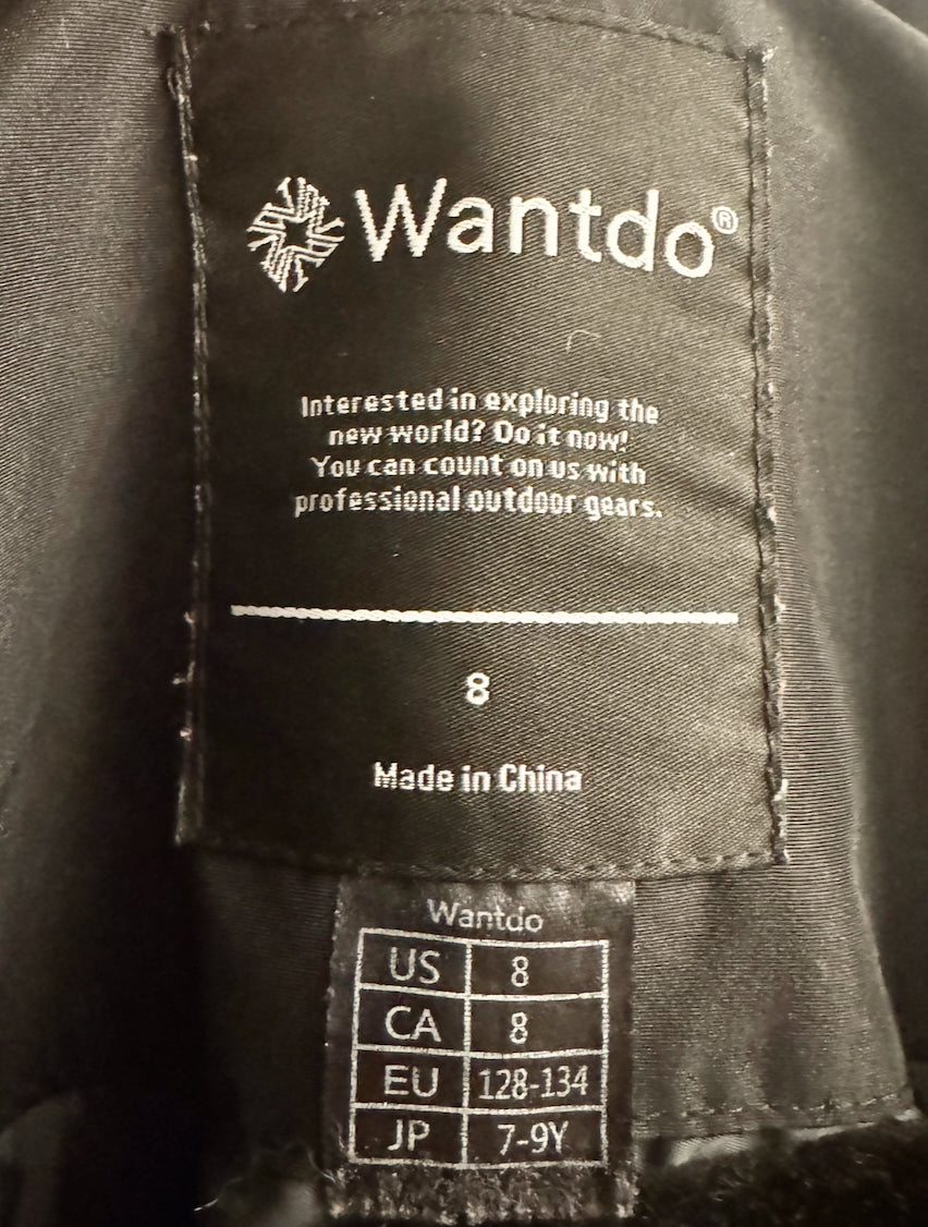 Close-up of a black Wantdo garment interior label showing the brand name, slogan, size 8, and country of origin, with a smaller size conversion chart below.