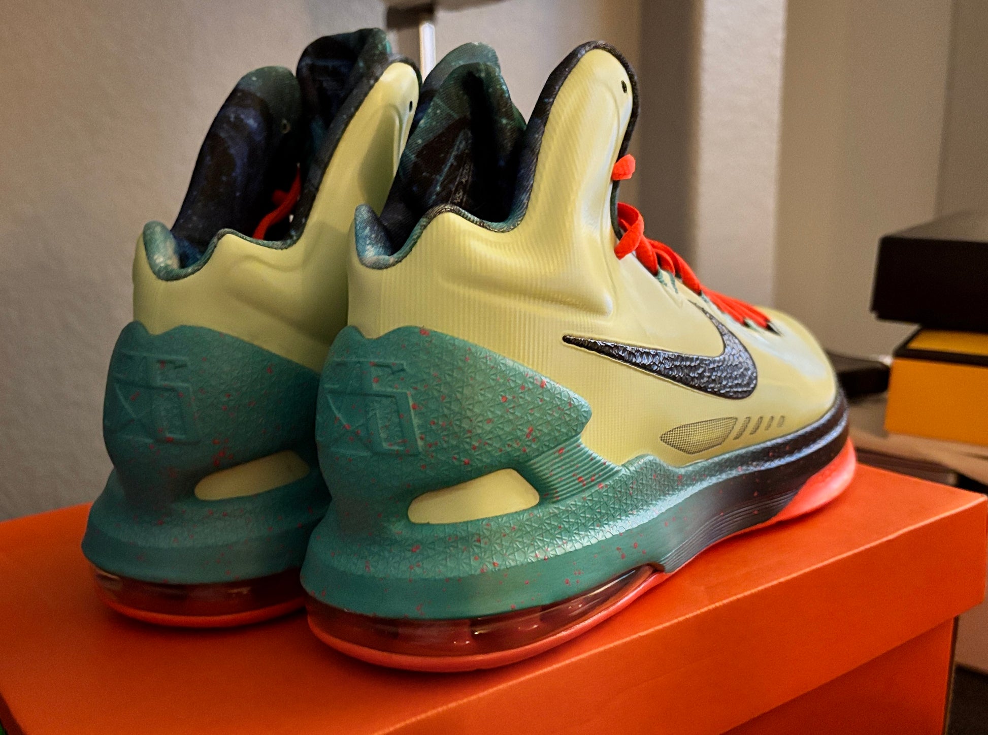 Pair of green and yellow sneakers on an orange surface with a neutral background