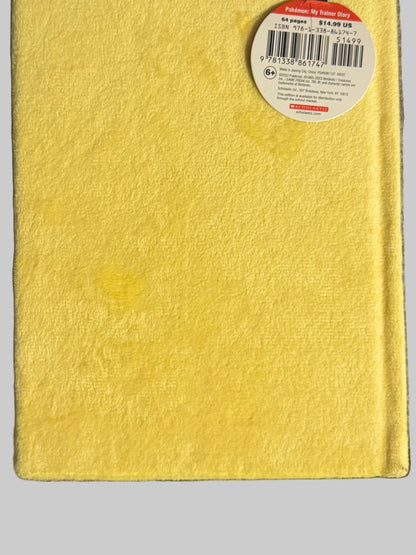 A bright yellow hardcover notebook with a black ribbon bookmark and a white product tag, laid flat on a textured gray fabric background.