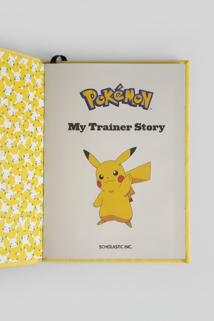 A Pokémon 'My Trainer Story' notebook or journal shown open, with the cover page featuring Pikachu and the Scholastic Inc. logo.