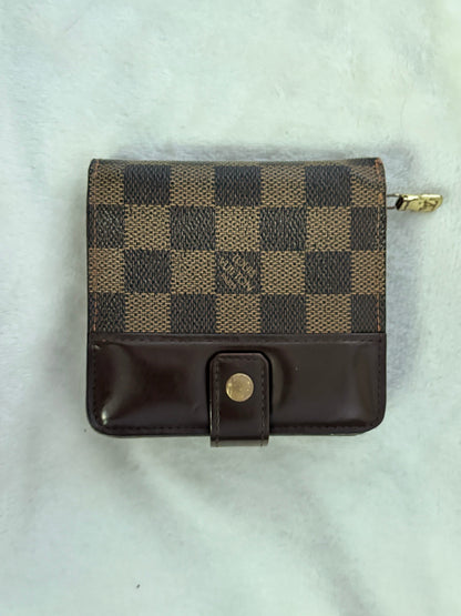 A small Louis Vuitton zip-around wallet in the Damier Ebene checkered canvas and dark brown leather, featuring a snap-button closure, laid flat on a white textured fabric background.