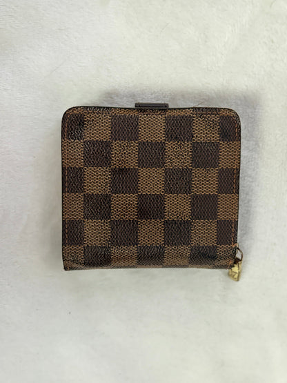 A small brown and tan checkered wallet with a gold zipper pull, placed on a white textured background.