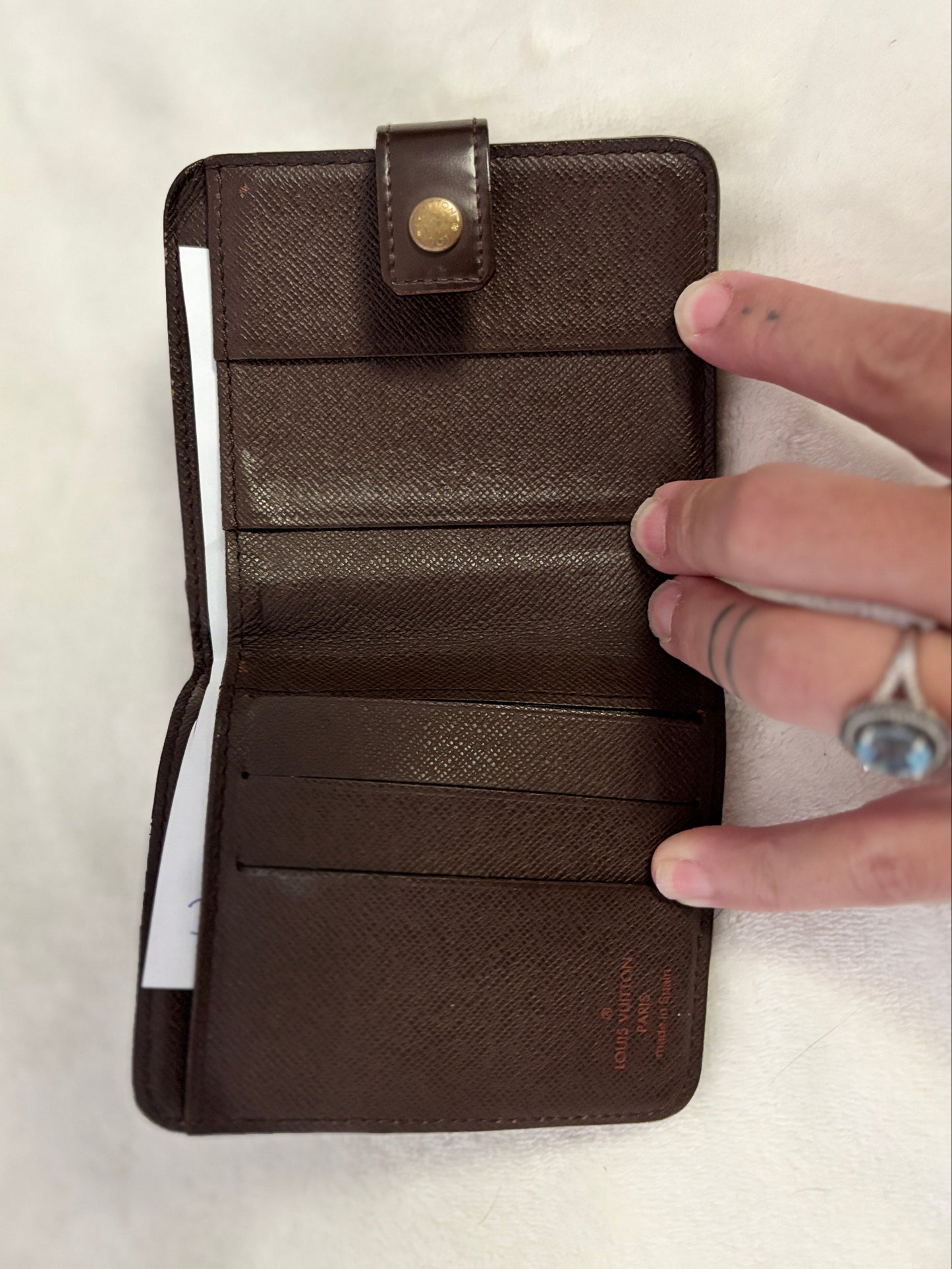 A dark brown textured leather wallet shown open, held by a hand on a light off-white fabric background.