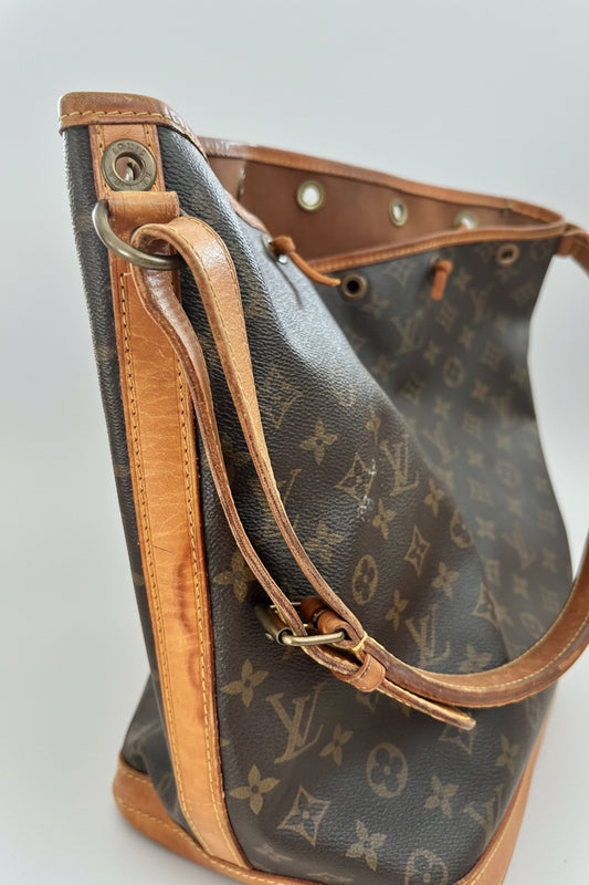 A Louis Vuitton monogram canvas shoulder bag with tan leather trim and strap, shown in a close-up shot against a light gray background.