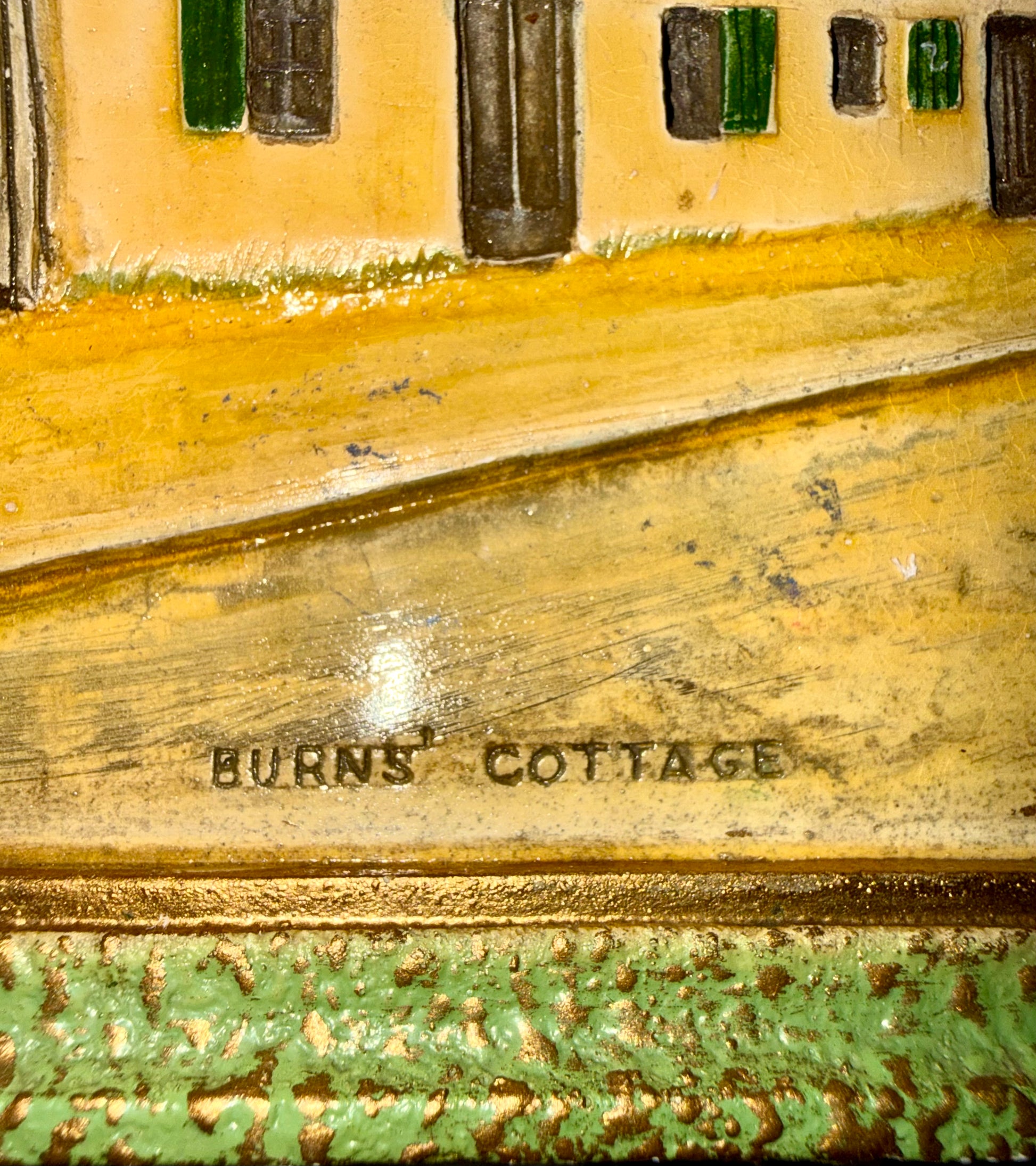 Close-up of a decorative plaque with 'Burns' Cottage' engraved on it, featuring a miniature landscape.