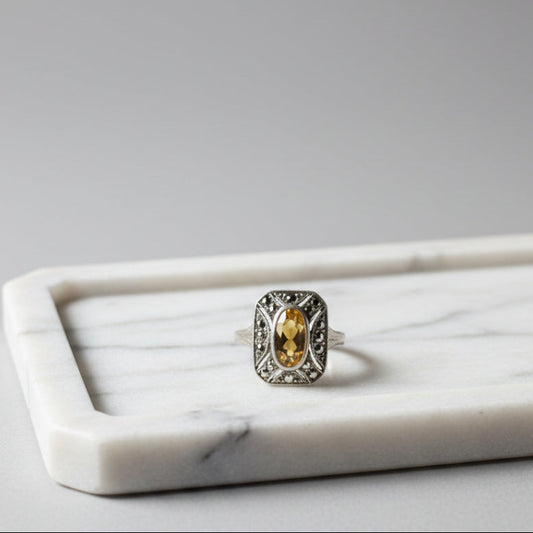 Silver ring with a yellow gemstone on a textured surface