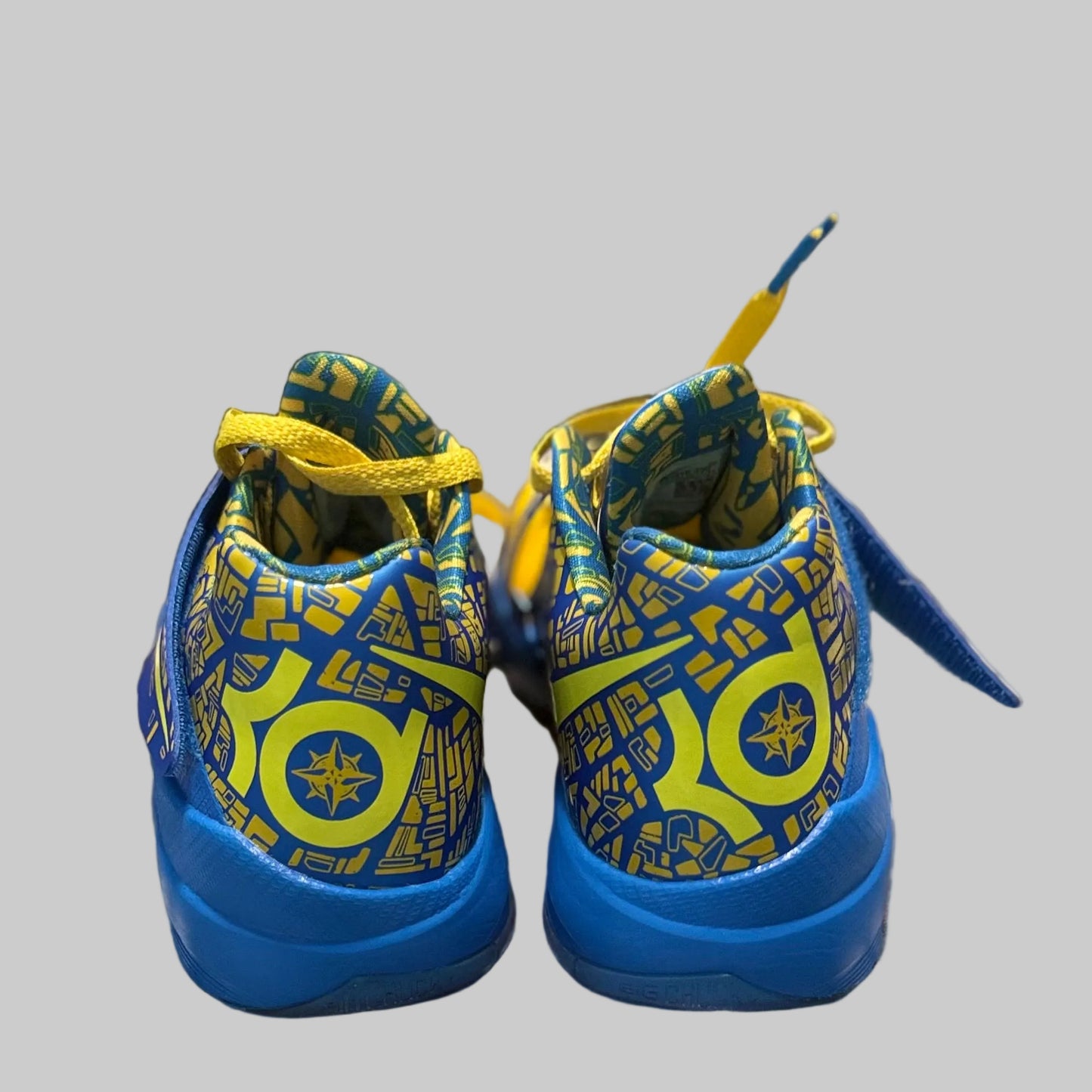 A pair of blue and yellow patterned sneakers placed on a gray and white plaid blanket in a bedroom setting.