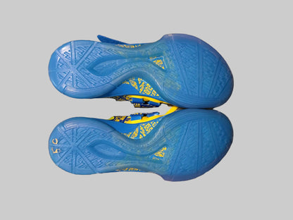 A pair of blue athletic shoes shown from the sole side, resting on a plaid blanket with a person's hand visible underneath for scale.