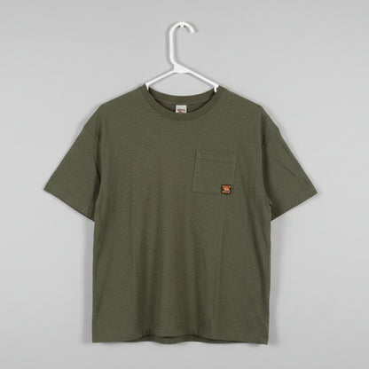 An olive green short-sleeve pocket t-shirt hanging on a white plastic hanger against a textured off-white wall.