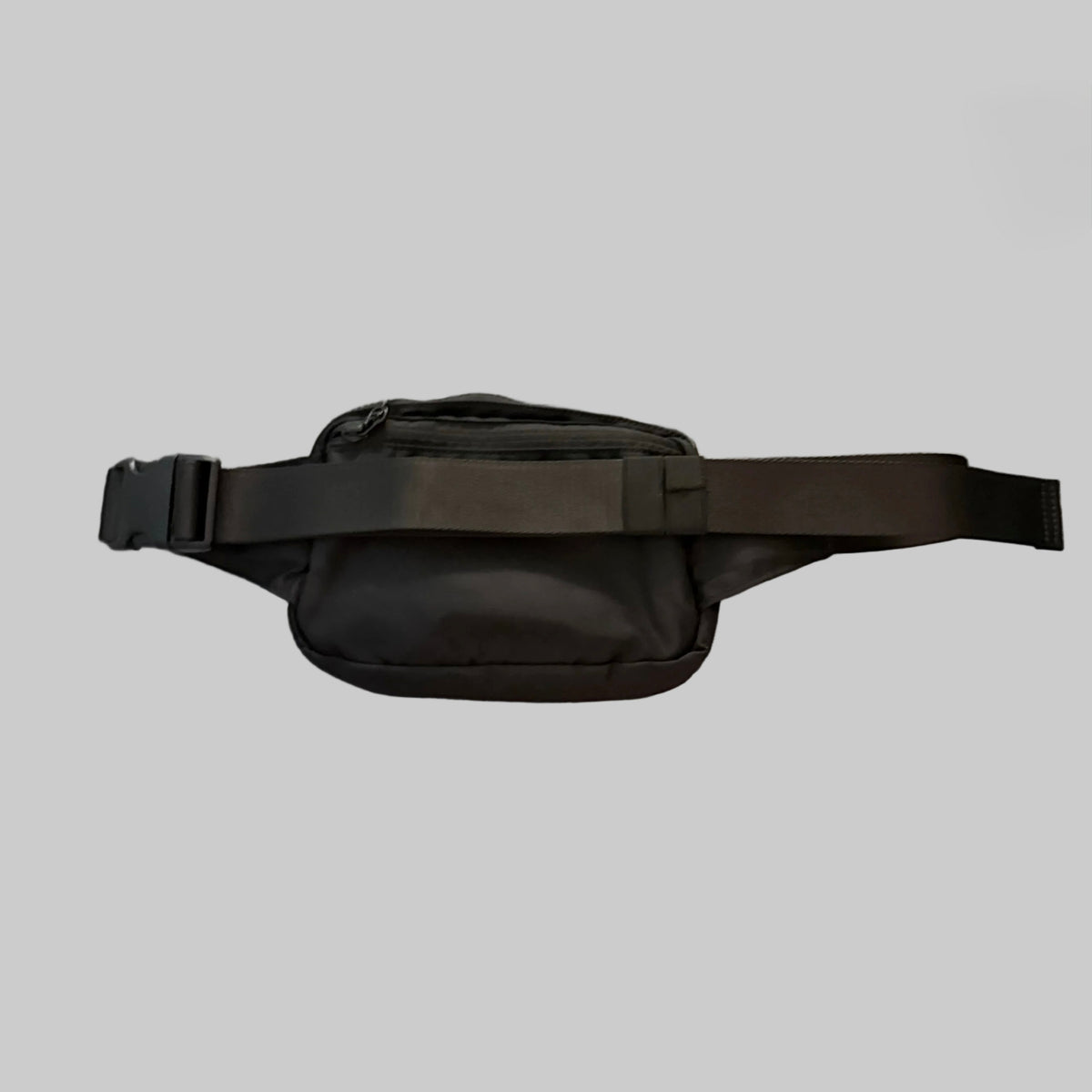 A black nylon fanny pack with a wide adjustable strap and plastic buckle, shown against a solid gray background.