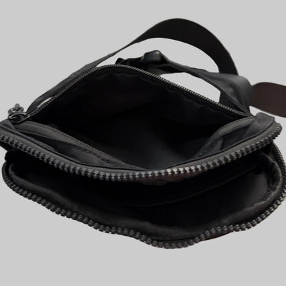 A black nylon crossbody bag shown open, displaying its interior lining and zipper compartments, set against a solid gray background.