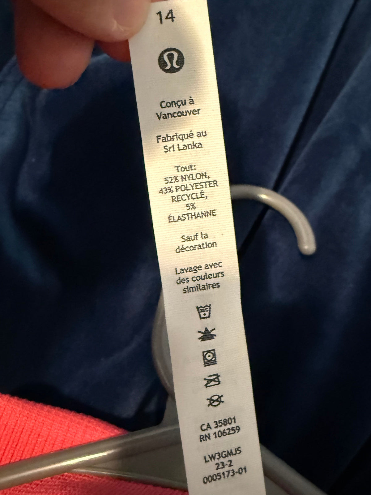 A close-up of a hand holding a white Lululemon garment care tag with French text, set against a dark blue fabric background.