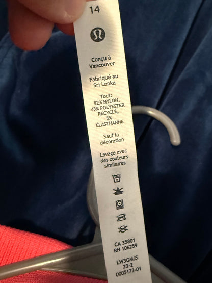 A close-up of a hand holding a white Lululemon garment care tag with French text, set against a dark blue fabric background.