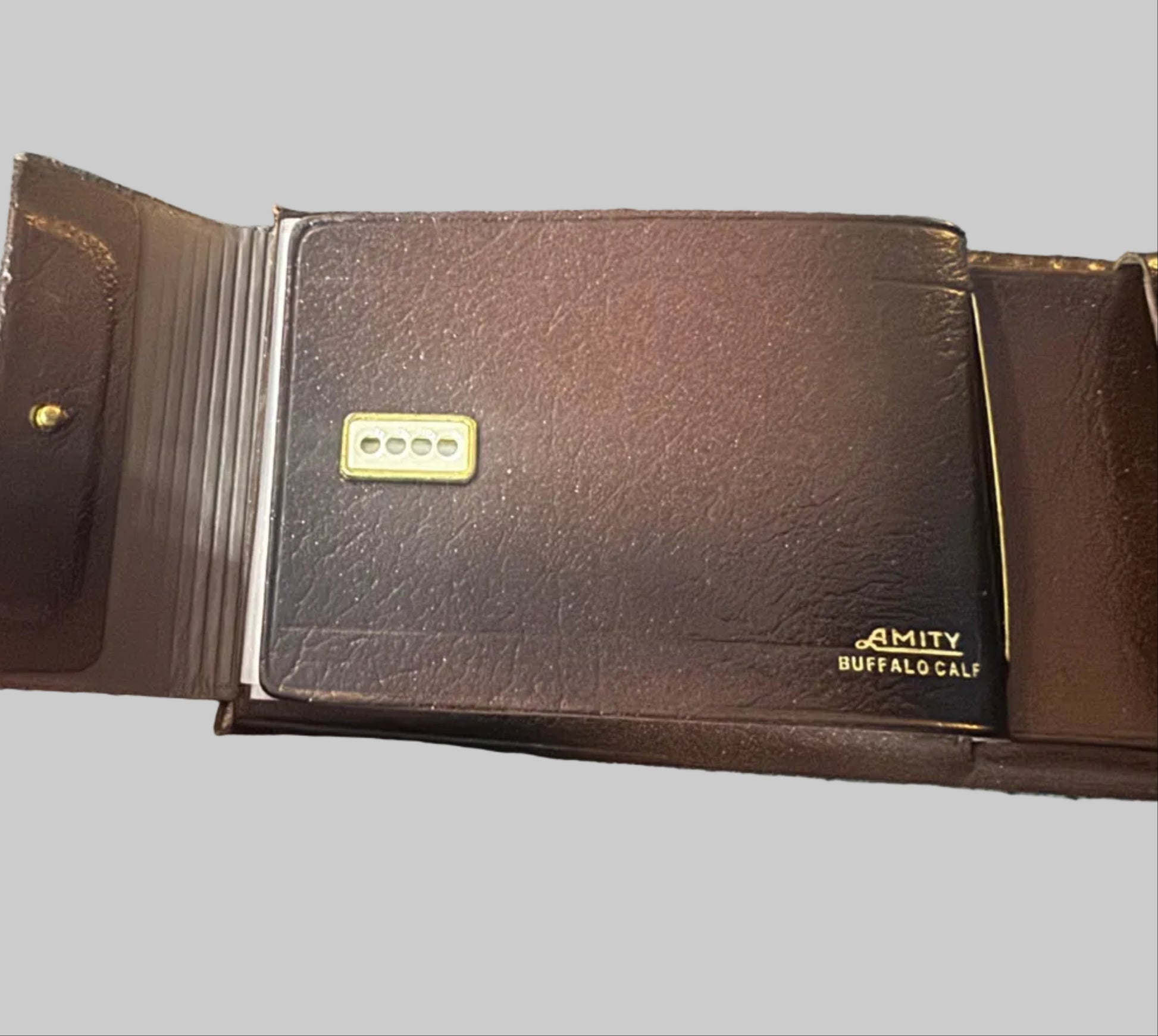 Brown leather wallet with 'Amity Buffalo' branding held by a hand on a textured surface.
