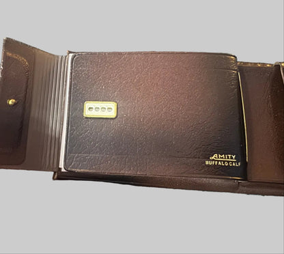 Brown leather wallet with 'Amity Buffalo' branding held by a hand on a textured surface.