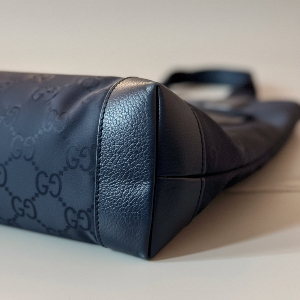 Close-up of a black leather handbag with a brand logo on a light surface.