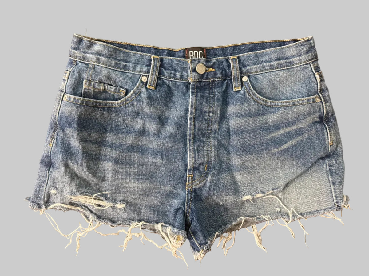 Light wash blue denim shorts with raw, frayed hems, laid flat on a dark wooden surface.