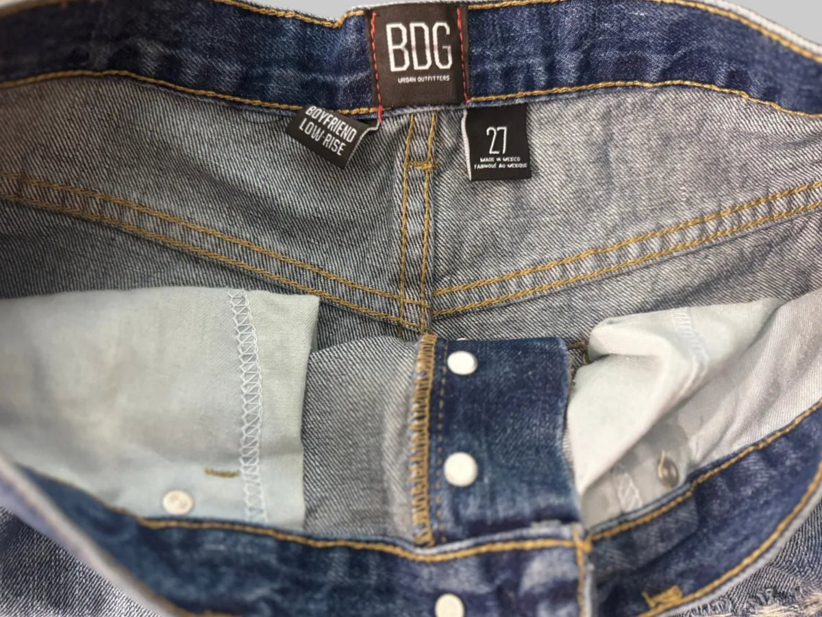 Close-up of the inner waistband and construction details of a pair of blue denim jeans, showing the waistband, buttonholes, inner pocket lining, and BDC brand labels.