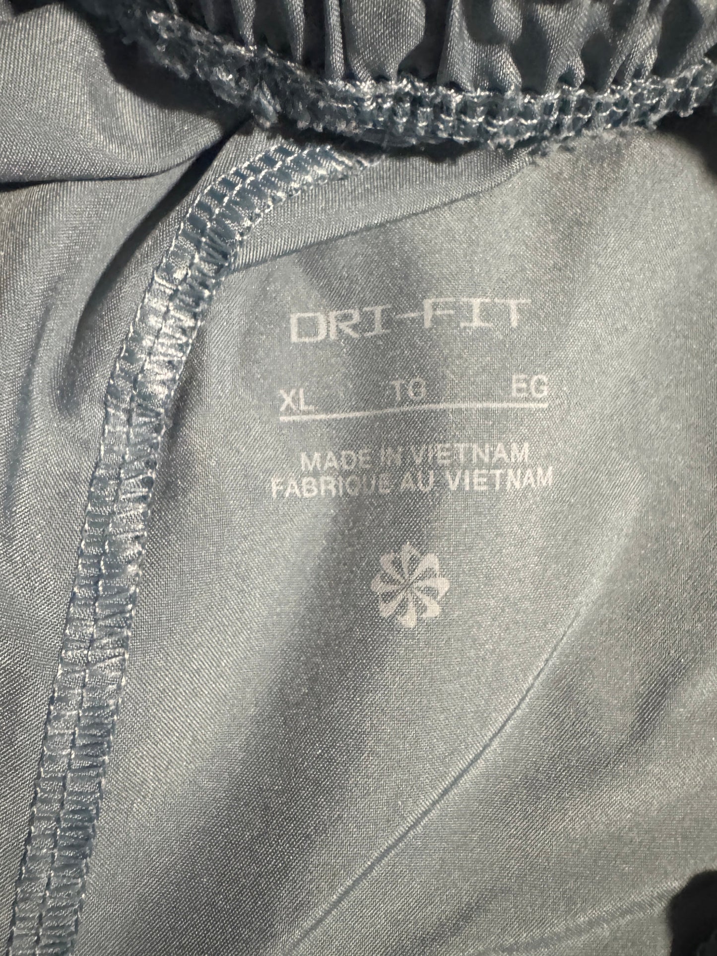 Close-up of the inside waistband of gray athletic pants, showing the elasticized drawstring waist, white printed size and material details, and a white logo.