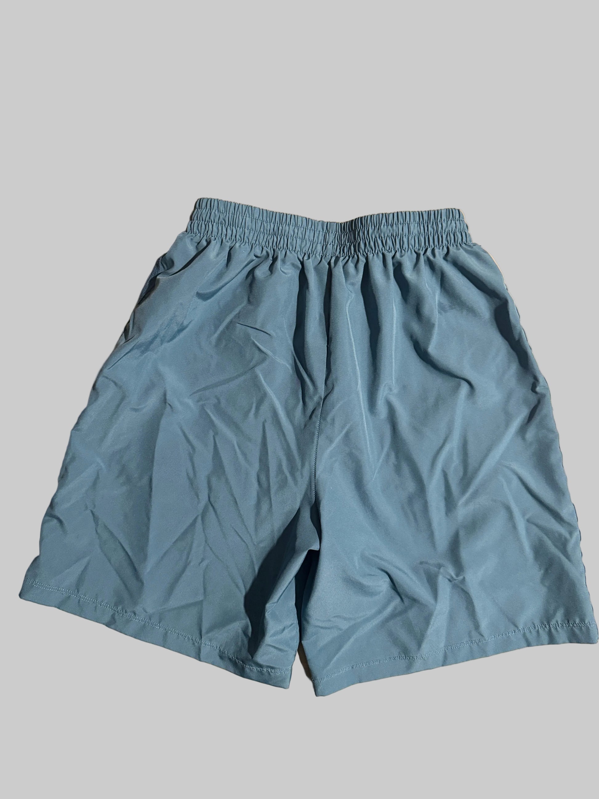 Light blue athletic shorts with an elastic waistband, laid flat on a light-colored wooden surface.