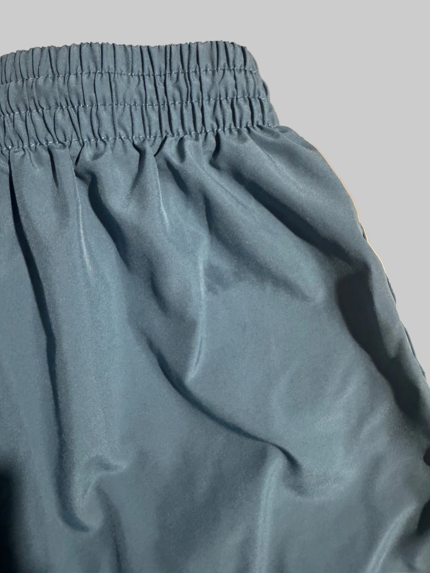 Close-up of a dusty slate blue fabric garment, showing a gathered elastic waistband on a beige tiled floor background.