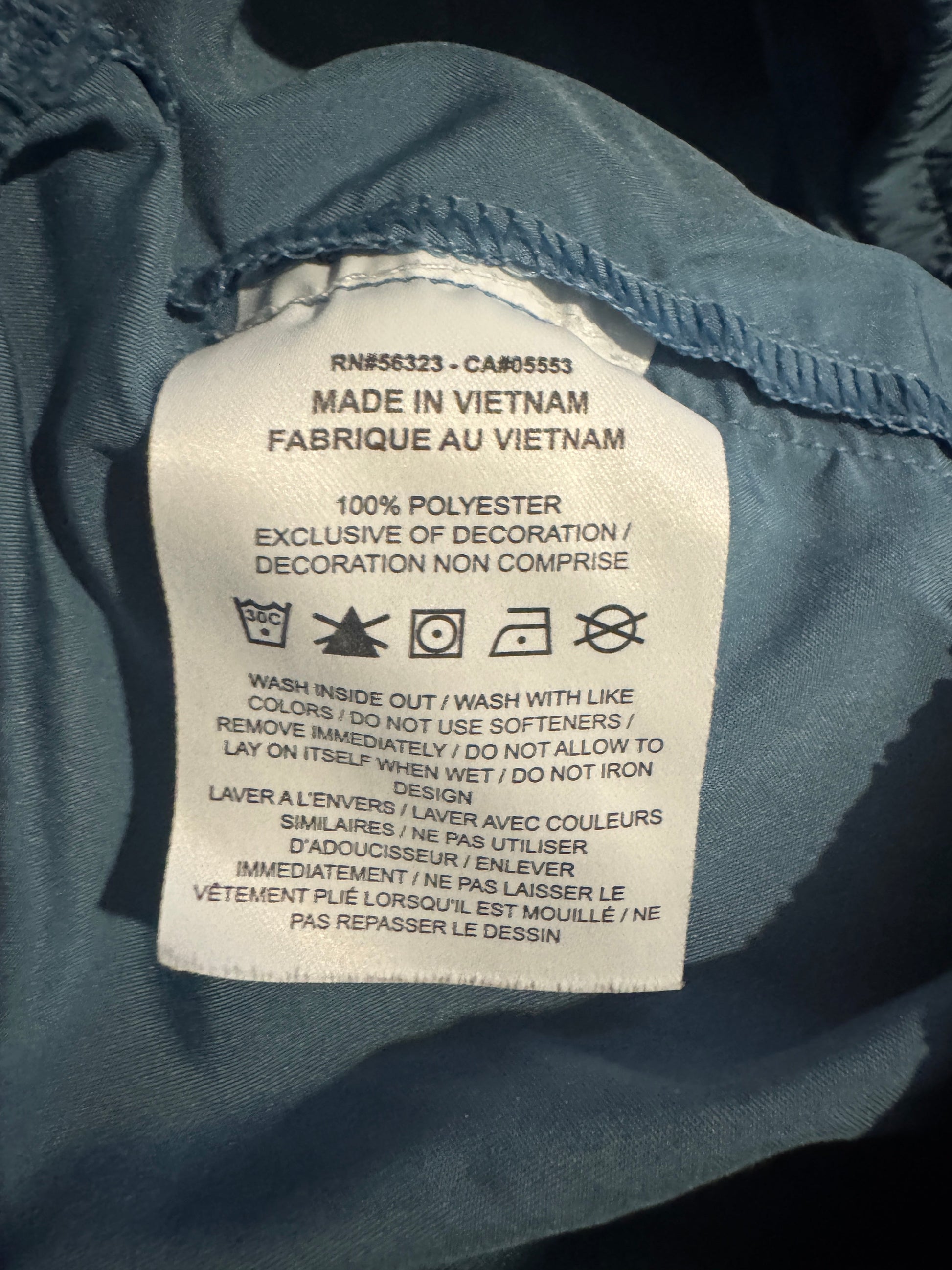 Close-up of a sewn-on white fabric care label inside a blue-gray garment, showing text including 'MADE IN VIETNAM' and care symbols.