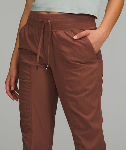 A close-up of a person wearing brown drawstring jogger-style pants with side pockets, paired with a pale mint green cropped top, against a solid gray studio background.
