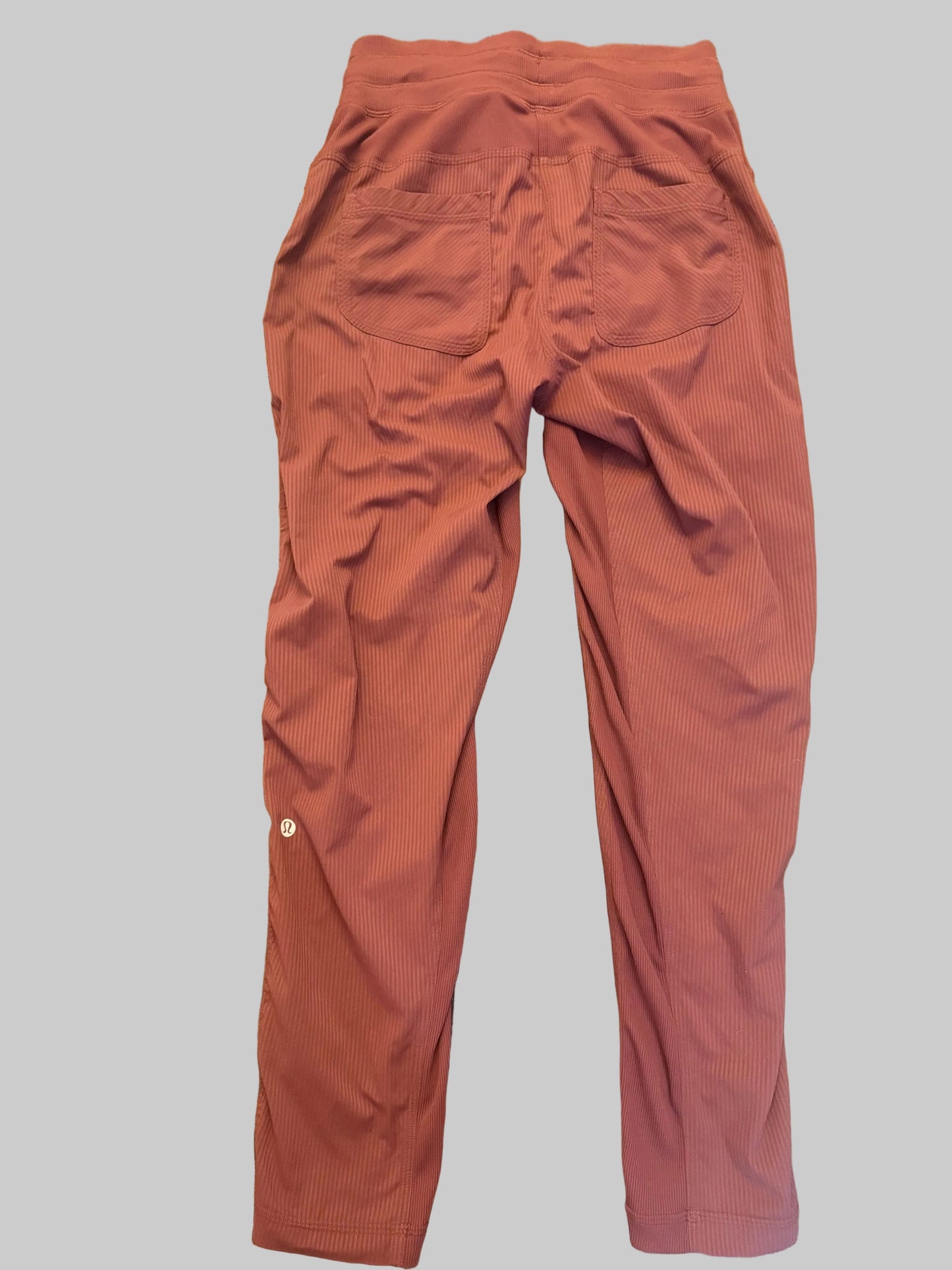 A pair of loose-fitting, rust-orange corduroy trousers laid flat on a solid gray background.