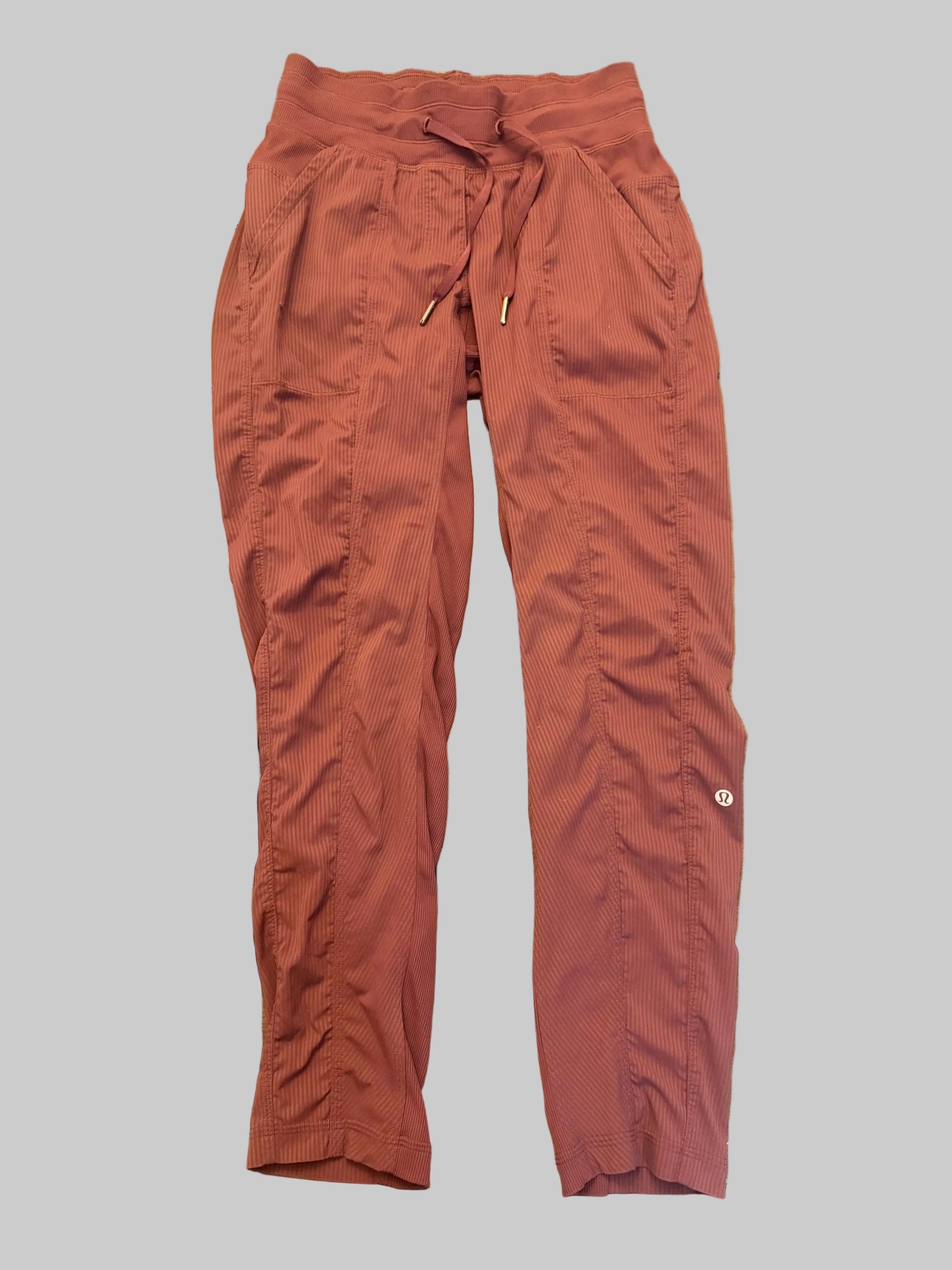 A pair of rust-colored drawstring pants laid flat on a wooden table.
