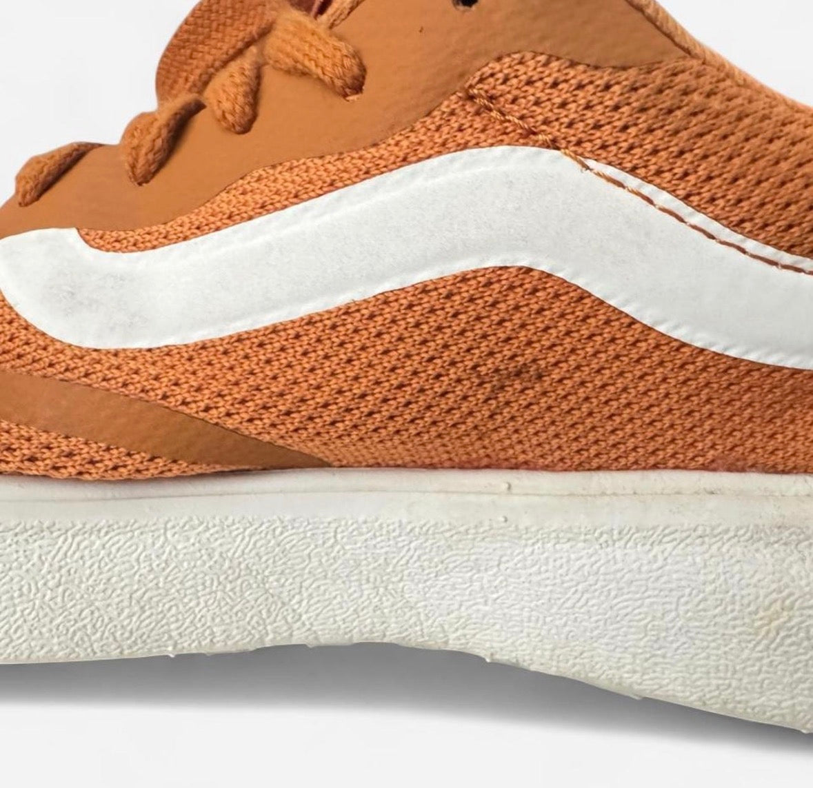 Close-up of a low-top sneaker showing the side profile, featuring an orange knit upper, a white wavy side stripe, and a thick white textured sole.