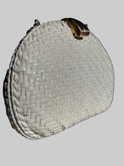 A white woven clutch purse with a gold-tone metal clasp, resting on a textured gray surface against a dark background.