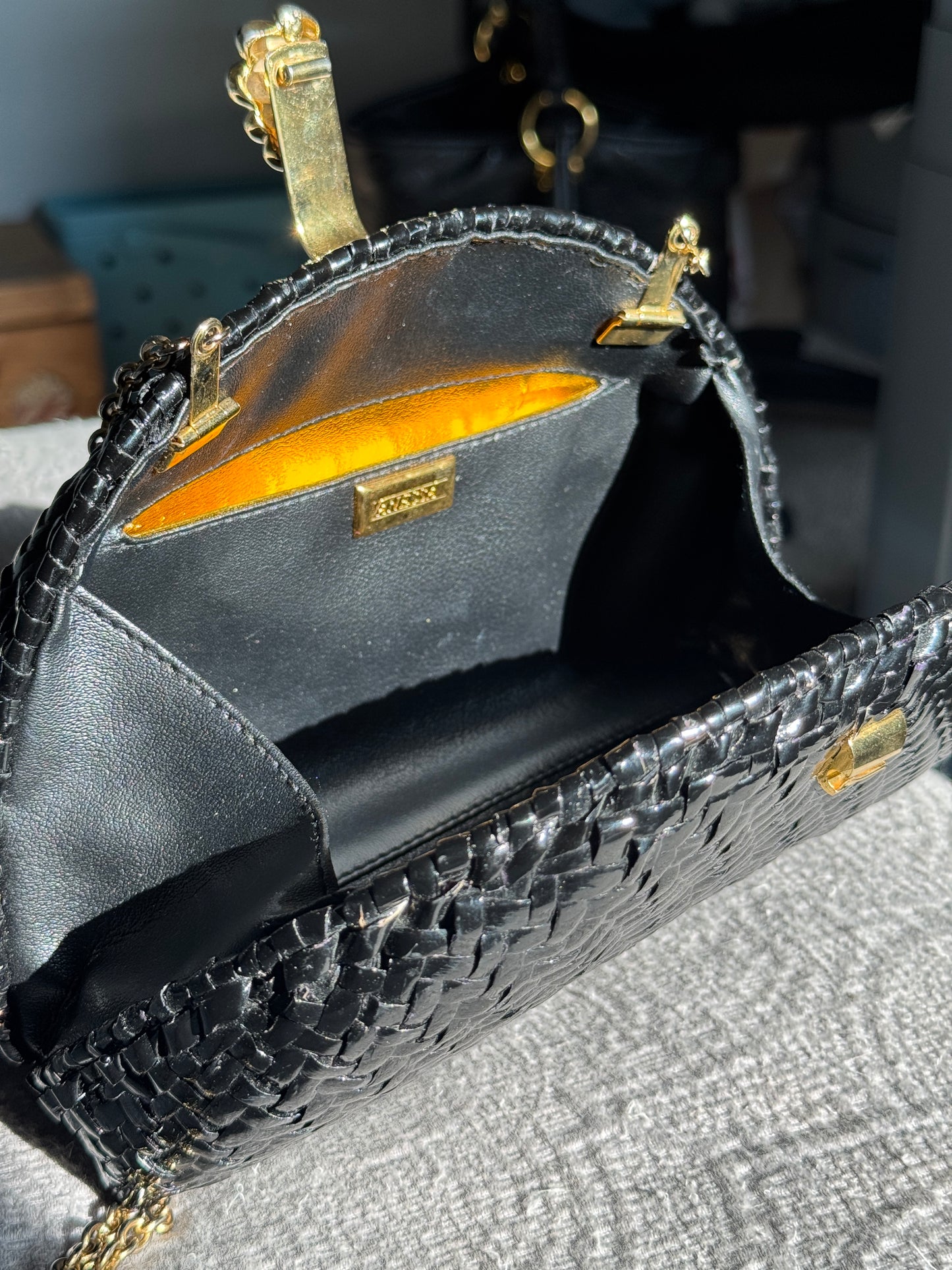 A close-up of a black woven leather handbag with gold-tone hardware, showing the interior lining and a small gold brand plaque.