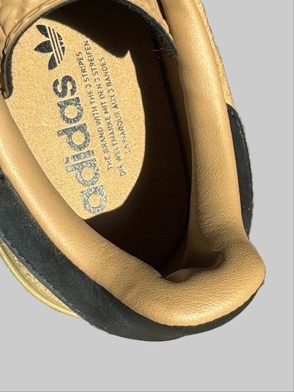 Close-up of the interior of an Adidas sneaker, showing the tan suede and leather lining with the Adidas trefoil logo and brand name printed on the insole.