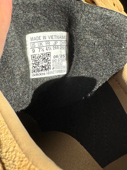 Close-up of the interior label of a tan sneaker, showing the Adidas brand name and size information.