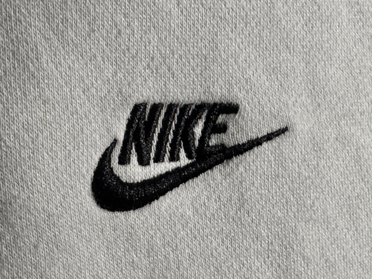 Close-up of a light gray knit fabric with a black embroidered Nike logo and swoosh.