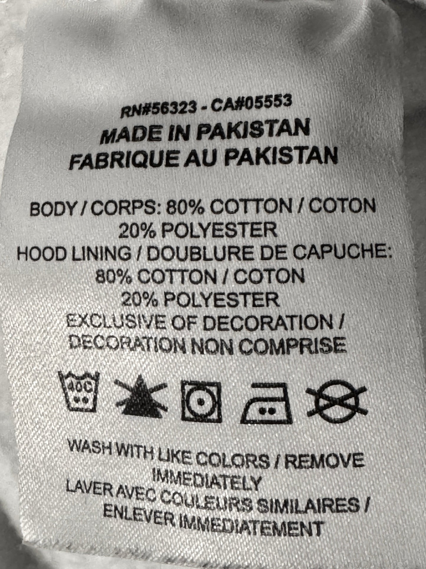 A close-up of a sewn-on fabric care label showing product details including 'Made in Pakistan' and material composition in cotton and polyester.