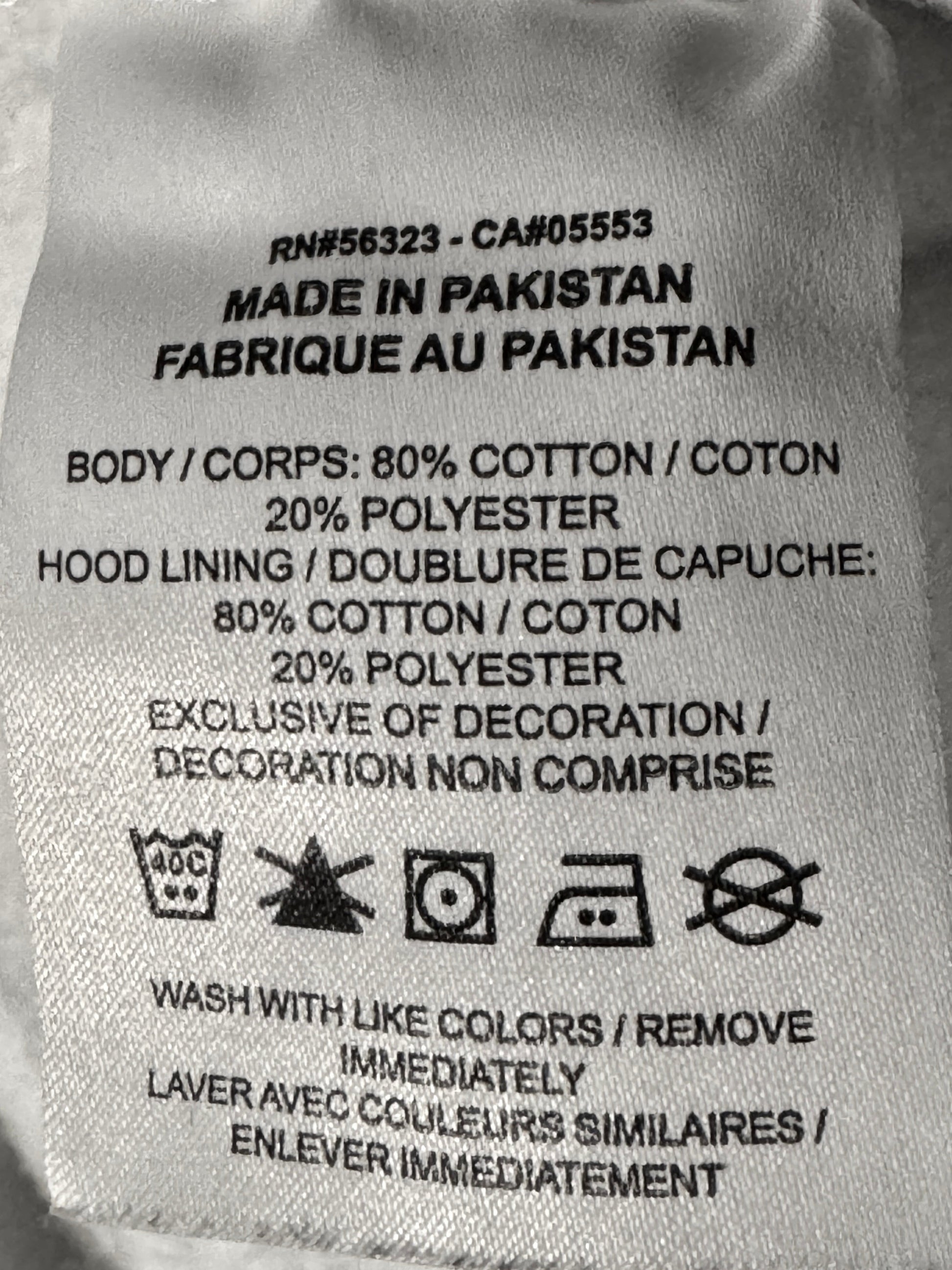 A close-up of a sewn-on fabric care label showing product details including 'Made in Pakistan' and material composition in cotton and polyester.