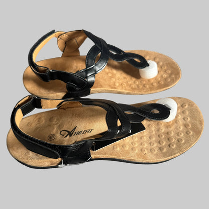 A pair of black leather strappy sandals with textured tan footbeds and white toe supports, displayed on a gray textured fabric background.