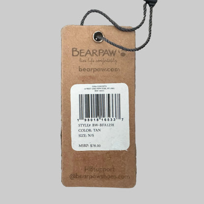 A brown cardboard product tag with a white barcode label, attached to a dark gray string, placed on a textured beige carpet. The tag shows the brand name BEARPAW and product details including color tan and size N/S.