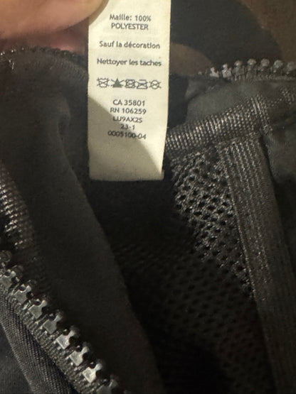 Close-up of a garment's interior label reading 'Molle: 100% POLYESTER' in French, attached to a black mesh zipper compartment.