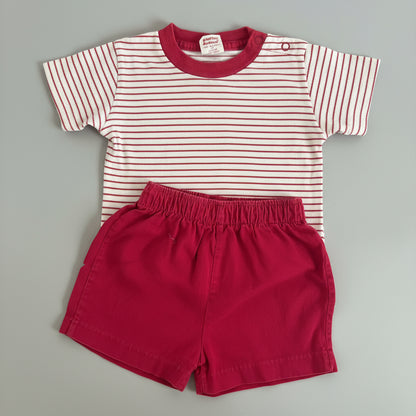A baby clothing set consisting of a short-sleeve top with red and white horizontal stripes and a solid red collar, paired with solid red shorts, laid flat on a gray textured blanket.