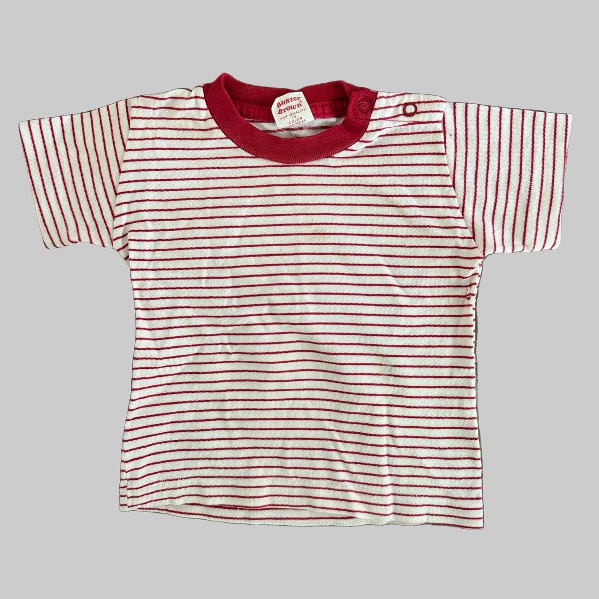A baby t-shirt with thin red horizontal stripes on a white background, featuring a solid red crew neck and a red snap button closure at the shoulder.