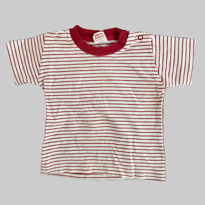 A baby t-shirt with thin red horizontal stripes on a white background, featuring a solid red crew neck and a red snap button closure at the shoulder.