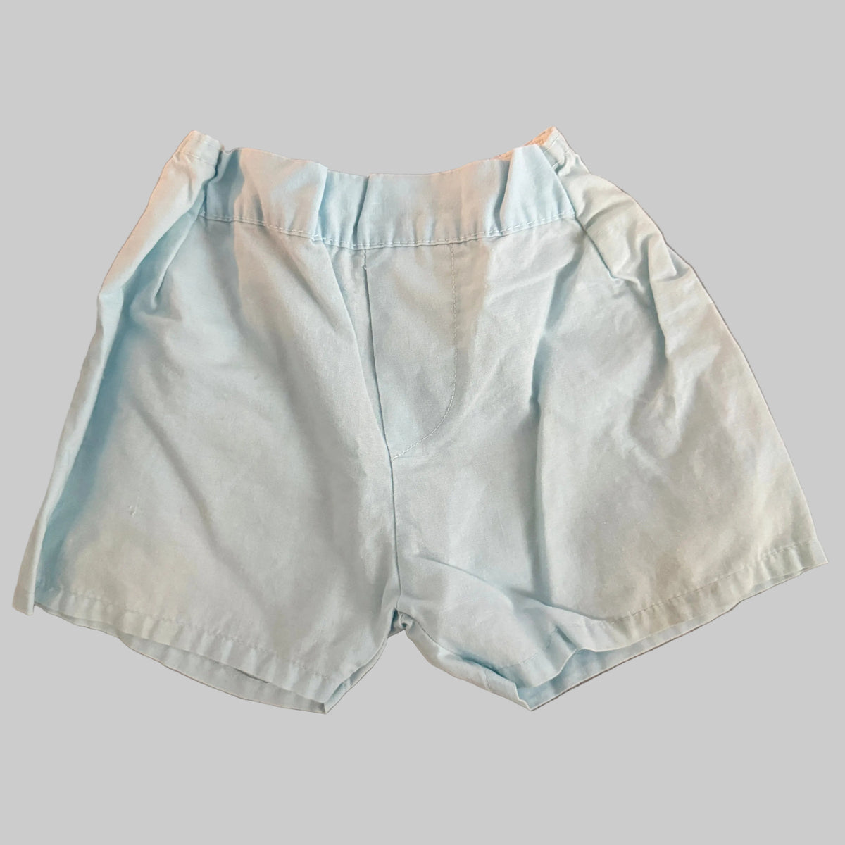 A pair of light blue cotton shorts laid flat on a textured brown fabric background.