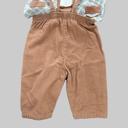 Toddler boy's corduroy overall in a warm tan-brown color, laid flat on a textured gray blanket with a light blue and white checkered shirt partially visible underneath.