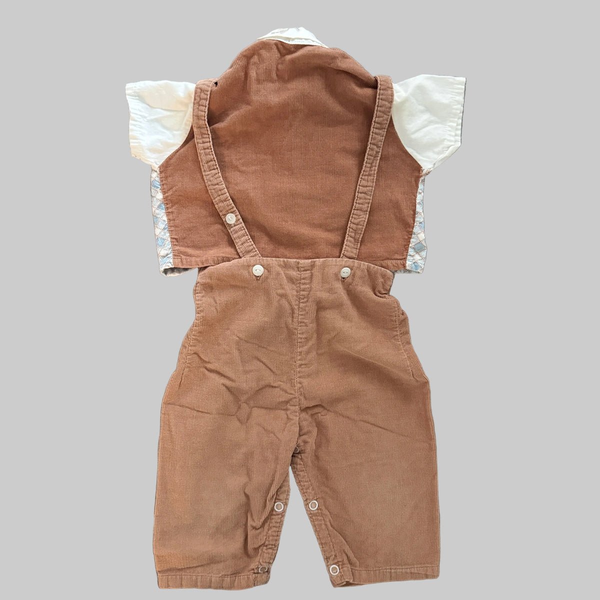 A baby's short-sleeve corduroy overall romper in a warm brownish-orange color, featuring a white ruffled shirt underneath, laid flat on a textured gray fabric background.
